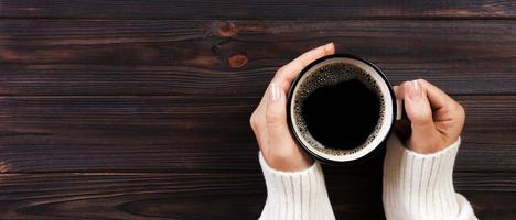 mujer solitaria tomando café por la mañana, vista superior de manos femeninas sosteniendo una taza de bebida caliente en un escritorio de madera. bandera foto