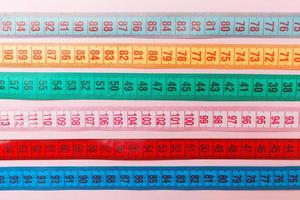 Close up of a group of colorful measure tapes lying in rows as a background. Diet concept on pink background photo
