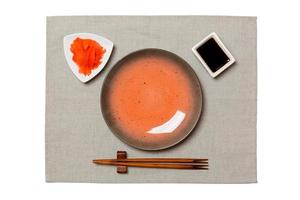 Empty round brown plate with chopsticks for sushi and soy sauce, ginger on grey napkin background. Top view with copy space for you design photo