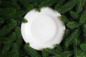 Top view of white plate surrounded with fir tree branches. Christmas dinner concept with copy space photo