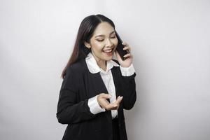 A portrait of a happy Asian businesswoman is smiling while talking on phone call wearing a black suit isolated by a white background photo