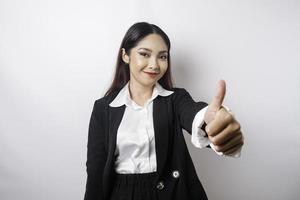 Excited Asian businesswoman wearing black suit gives thumbs up hand gesture of approval, isolated by white background photo