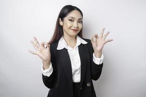 Excited Asian business woman wearing a black suit giving an OK hand gesture isolated by a white background photo