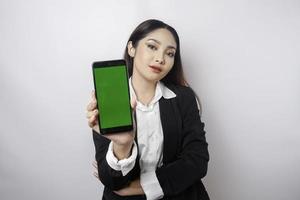A happy young businesswoman is wearing black suit, showing copy space on her phone isolated by white background photo