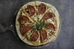 A portrait of a tasty pepperoni pizza on a wooden pan isolated by grey concrete background photo