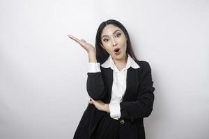 Shocked Asian businesswoman wearing black suit pointing at the copy space on top of her, isolated by white background photo