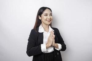 A smiling young Asian woman employee wearing a black suit gestures a traditional greeting isolated over white background photo