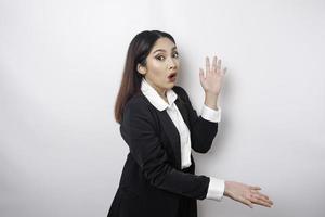 una mujer de negocios asiática sorprendida con un traje negro que señala el espacio de la copia a su lado, aislada por un fondo blanco foto