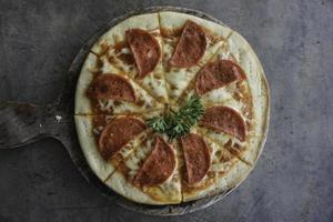 un retrato de una sabrosa pizza de pepperoni en una sartén de madera aislada por un fondo de hormigón gris foto