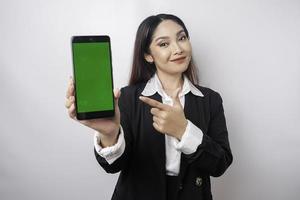 una joven empresaria feliz lleva traje negro, mostrando espacio de copia en su teléfono aislado por fondo blanco foto