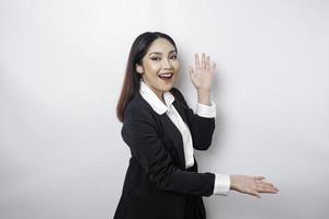 Excited Asian businesswoman wearing black suit pointing at the copy space beside her, isolated by white background photo