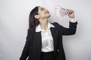 A happy young businesswoman is wearing black suit and holding cash money in Indonesian rupiah isolated by white background photo