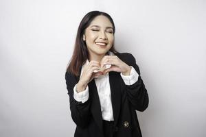 An attractive young Asian woman wearing a black suit feels happy and a romantic shapes heart gesture expresses tender feelings photo