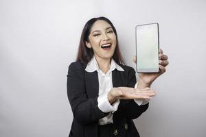 A happy young businesswoman is wearing black suit, showing copy space on her phone isolated by white background photo