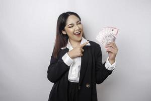 A happy young businesswoman is wearing black suit and holding cash money in Indonesian rupiah isolated by white background photo