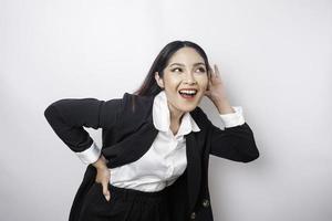 Amazed curious young woman wearing a black suit trying to hear you overhear listening intently isolated on a white background studio portrait. photo