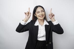 emocionada mujer de negocios asiática con traje negro apuntando al espacio de copia encima de ella, aislada de fondo blanco foto