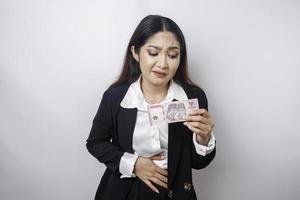 Photo of a hungry excited young businesswoman holding money in Indonesian Rupiah and wondering what to order yummy food isolated on white color background