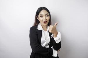 Excited Asian businesswoman wearing black suit gives thumbs up hand gesture of approval, isolated by white background photo