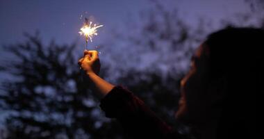 mise au point sélective un feu d'artifice brûlant dans la main d'une femme au festival du nouvel an, elle lève et agite la main pour jouer à la main scintillante le soir de la fête du nouvel an video