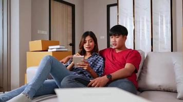 Zeitlupenaufnahme, junges Paar sitzt auf dem Schlafsofa und checkt die Liste, während es die Kisten nach dem Umzug in ihr neues Zuhause zählt, neues Hauskonzept video
