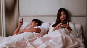 ralenti, jeune couple allongé sur le lit dans la chambre, ils s'amusent avec les réseaux sociaux les accros surfent sur internet sur les téléphones portables en s'ignorant, le concept de smartphone accro à la famille video