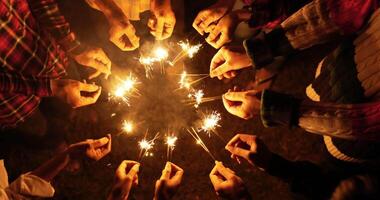 toma de mano en la parte superior, un grupo de jóvenes amigos se paran en círculo sosteniendo fuego quemando bengalas, están levantando y saludando jugando con chispas en las manos en la noche de fiesta de año nuevo al aire libre video