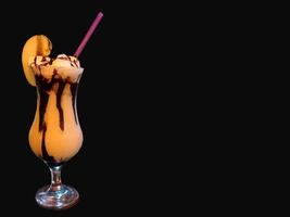 Glass with green apple drink, condensed milk and chocolate sauce with a straw on a black background and copy space photo