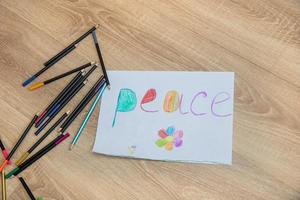 on the floor lies a children's drawing and colored pencils nearby, the word peace is written and painted on the drawing photo