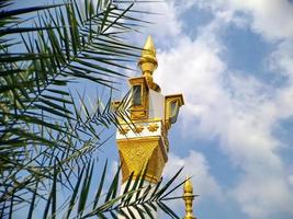 minarete de mezquita de color blanco dorado marrón con arquitectura árabe en el parque madiun indonesia, clima soleado. foto