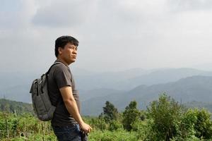 A sian man with his backpack and camera is travel alone and look at far a way, nature travel and environment concept, copy space for individual text photo