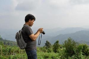 A sian man with his backpack and camera is travel alone and check his image, nature travel and environment concept, copy space for individual text photo