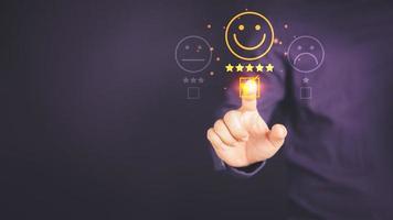 Man touching the virtual screen on the happy smiley face icon to give satisfaction in service. Rating very impressed. Customer service, testimonial satisfaction concept. photo