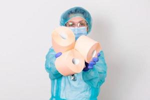 Doctor wearing PPE protection suite or nurse with a stethoscope holds a rolls of toilet paper. Lack of toilet paper in the quarantine of coronavirus, the concept of a shortage of things in stores photo