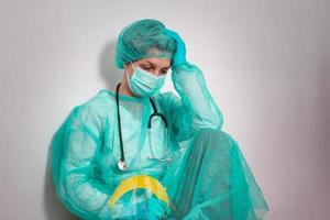 concepto de coronavirus. COVID-19. joven doctora con uniforme de traje protector, mascarilla y guantes de goma, antes de que el examen del paciente se sienta exhausto y preocupado. los médicos son héroes. foto