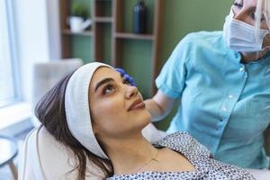 Concept of relaxation and body care. Top angle portrait of female therapist making anti-age massage of forehead wrinkles to young woman in spa salon photo