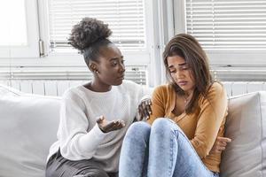 chica triste y amigos de apoyo tratando de resolver un problema. dos tristes mujeres diversas hablando en casa. amigas apoyándose mutuamente. problemas, amistad y concepto de cuidado foto