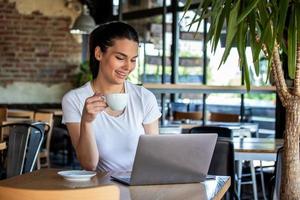 Woman in a good mood with cup of coffee sitting in cafe. Bright sunny morning. Gorgeous female drinking coffee and surfing the net in the coffee break. Morning coffee is my daily routine photo