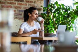 Woman in a good mood with cup of coffee sitting in cafe. Bright sunny morning. Gorgeous female drinking coffee and surfing the net in the coffee break. Morning coffee is my daily routine photo