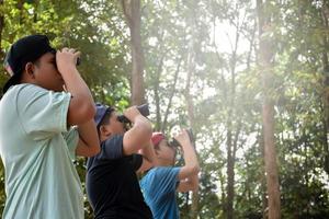 retrato de niños asiáticos usando binoculares para observar aves en el bosque tropical con sus amigos, idea para aprender criaturas y animales salvajes fuera del aula, enfoque suave. foto