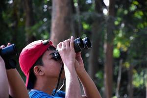 Portrait Asian boys using binoculars to watch birds in tropical forest with his friends, idea for learning creatures and wildlife animals outside the classroom, soft focus. photo