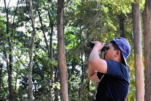 Portrait Asian boys using binoculars to watch birds in tropical forest with his friends, idea for learning creatures and wildlife animals outside the classroom, soft focus. photo