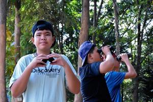 Portrait Asian boys using binoculars to watch birds in tropical forest with his friends, idea for learning creatures and wildlife animals outside the classroom, soft focus. photo