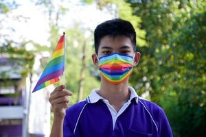 Portrait Asian young boy holds rainbow flag, LGBT symbol, in hands while joining his LGBT activity at school, concept for LGBT community celebration in pride month, June, 2023, around the world. photo