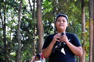 Portrait Asian boys using binoculars to watch birds in tropical forest with his friends, idea for learning creatures and wildlife animals outside the classroom, soft focus. photo