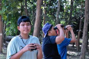 retrato de niños asiáticos usando binoculares para observar aves en el bosque tropical con sus amigos, idea para aprender criaturas y animales salvajes fuera del aula, enfoque suave. foto