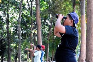 retrato de niños asiáticos usando binoculares para observar aves en el bosque tropical con sus amigos, idea para aprender criaturas y animales salvajes fuera del aula, enfoque suave. foto