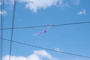 a broken kite stuck in a power line is dangerous because it will create a short circuit, isolated in the blue sky photo