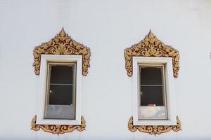 Golden and red color frame of white painted wood windows on white painted cement wall in ancient native Thai style of building in temple in Bangkok, Thailand. photo