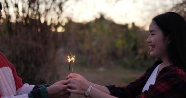 mulher bonita asiática recebe fogos de artifício queimando diamante do namorado por tocar no festival de ano novo, vestido com camisa xadrez, acenando com as mãos, eles riem e se divertem na noite de festa de ano novo video